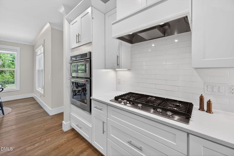 Modern kitchen with white shaker cabinets, stainless steel double oven, gas cooktop, white subway tile backsplash, and hardwood floors.