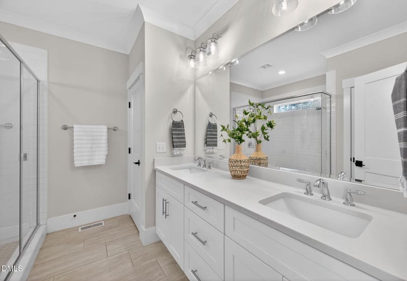 Modern bathroom with white double vanity, quartz countertop, large mirror with vanity lights, glass shower, and light wood floors.
