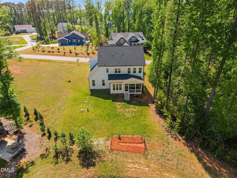 Aerial view of white two-story house with dark roof on large green lawn with trees and small garden plot.